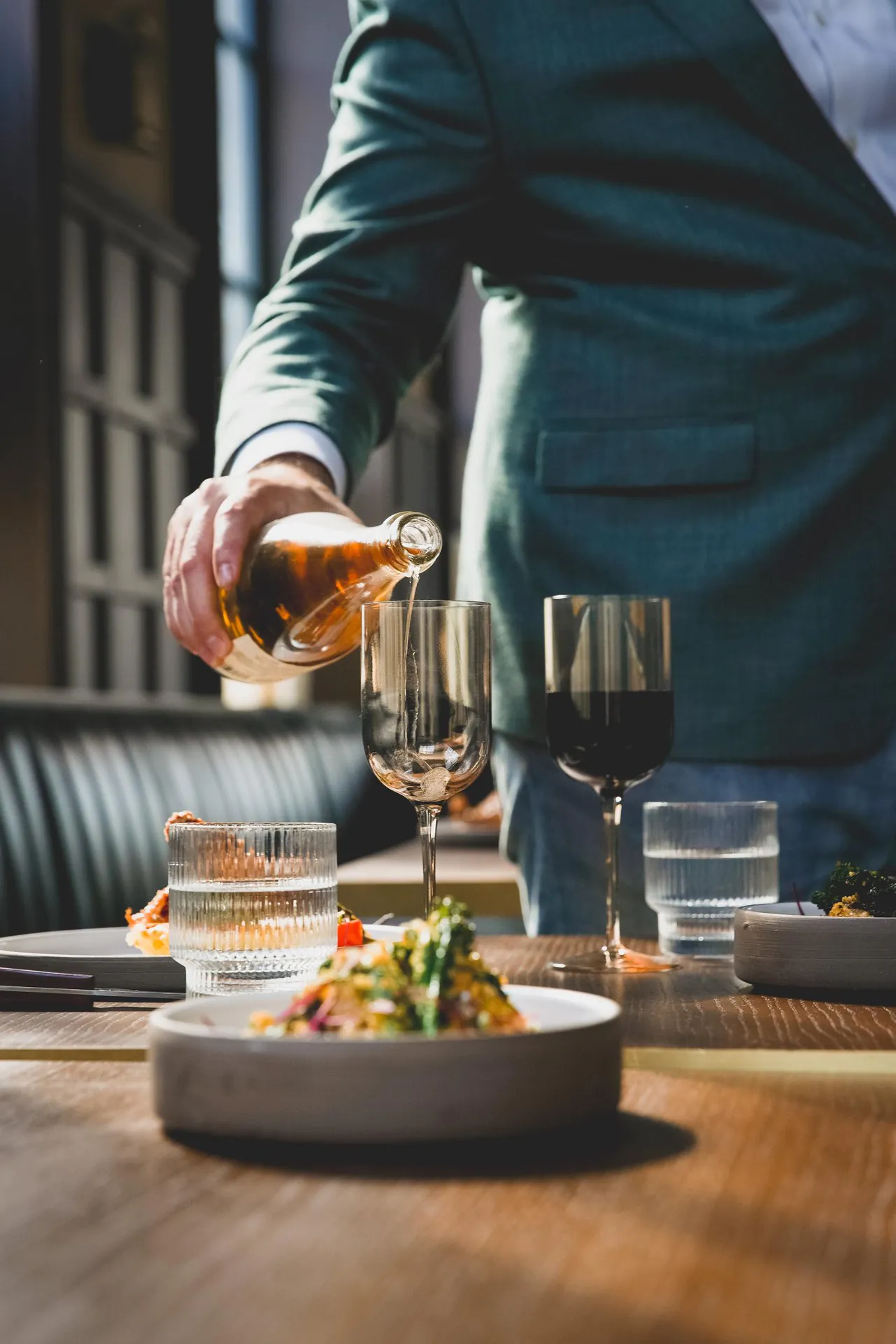fine dining tablescape with entree and man pouring wine into a wine glass