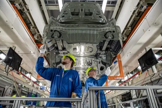 Two manufacturing workers at the Toyota plant examine the metal skeleton of a car.