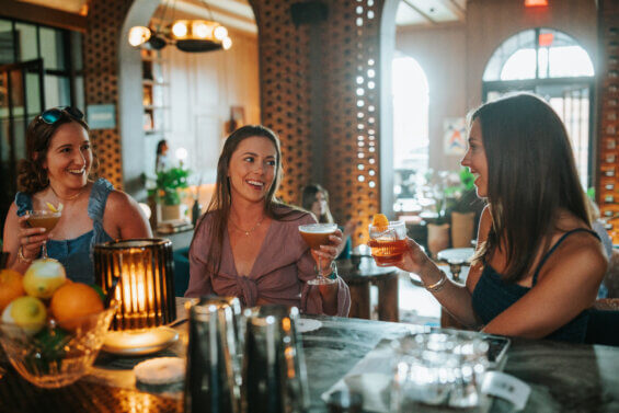 Three women clink glasses at a bar.