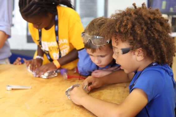 Small children work on an activity at a table together.