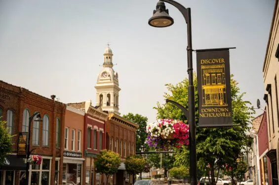 A lamppost sign on a quaint street reads "Discover Downtown Nicholasville" with historic buildings in the background.